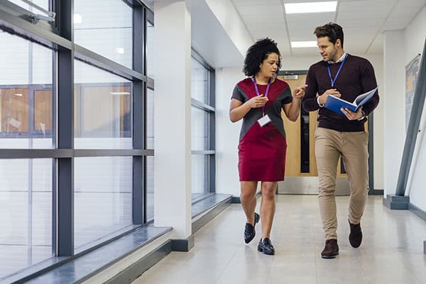 A pair of education administrators having a conversation while walking down a hallway.