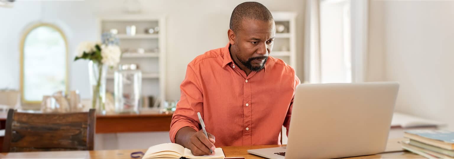 Man taking notes while looking at a laptop.