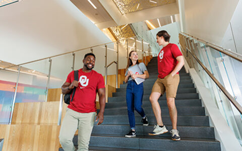 Decorative photo of three OU students wearing crimson shirts and walking down stairs