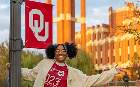 Smiling black student next to an OU banner on a lamppost near Bizzell Library