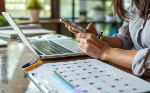 laptop and calendar on table with student holding iphone and pen