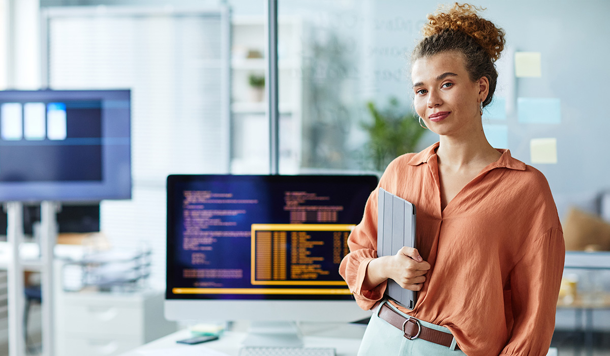 smiling computer science professional holding tablet and standing in front of multiple computers