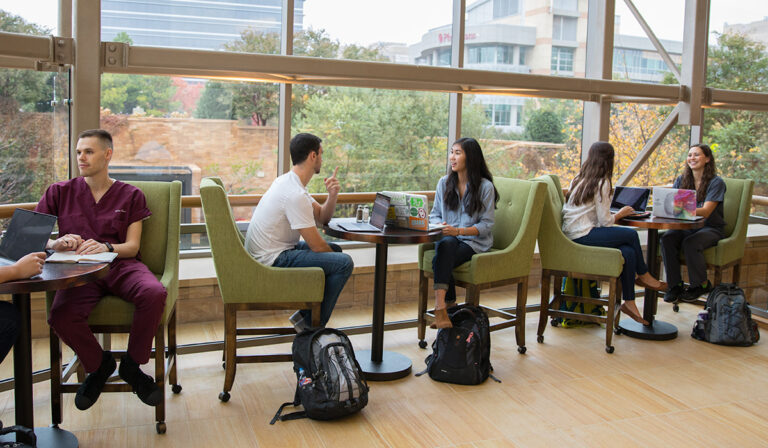 students sitting at a table in front of large windows