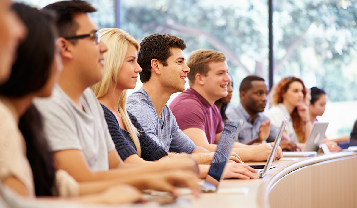 row of several students with laptops in a lecture hall