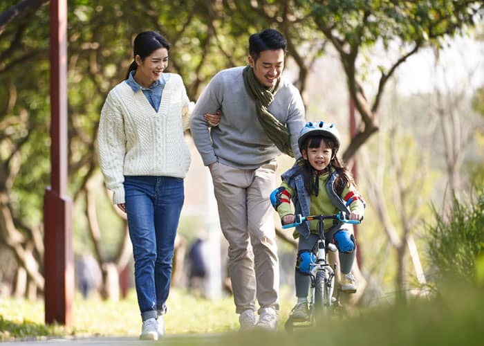 decorative image of Asian family in the park with child riding her bike