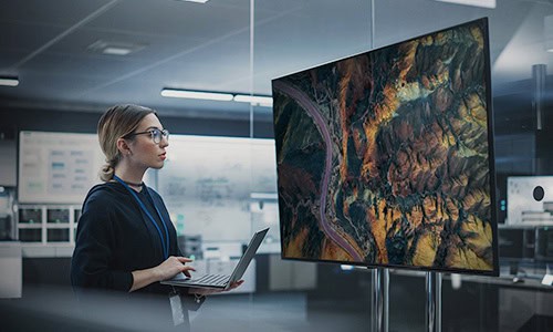 decorative image of young woman viewing geospatial map on her computer screen