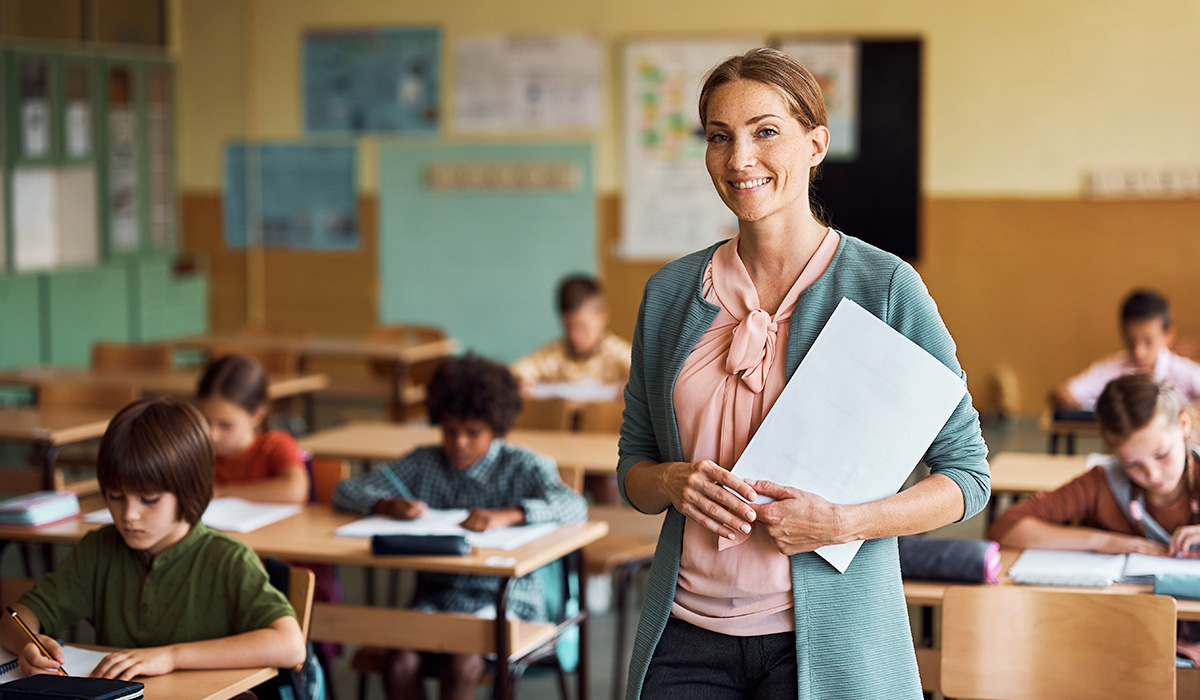 teacher standing at the front of the classroom while student work on their assignment