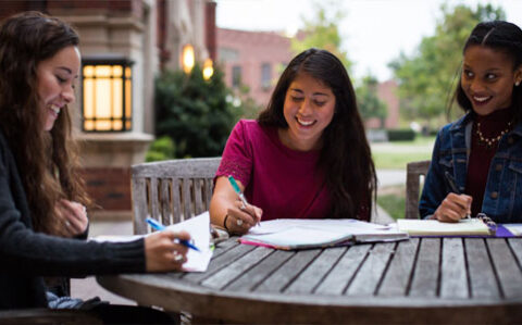 3 female students working on a course assignment at am outside table near the Oklahoma Memorial Union