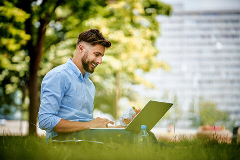 A man working on a laptop in a pleasant outdoors setting.