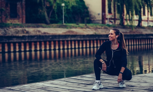 woman sitting on a wooden pathway putting on her running shoes