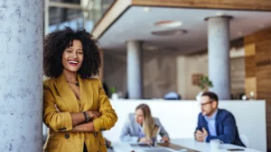 Smiling business leaders leaning against a pillar while 2 co-workers are discussing a project