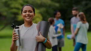 Smiling young woman in a park holding her yoga mat and water bottle