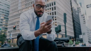 Business executive sitting outside in a large city checking meeting notes on his phone