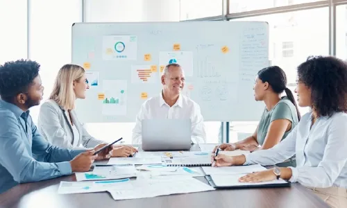 Five data professional sitting at a meeting table with several data documented in the table and on the white board behind them