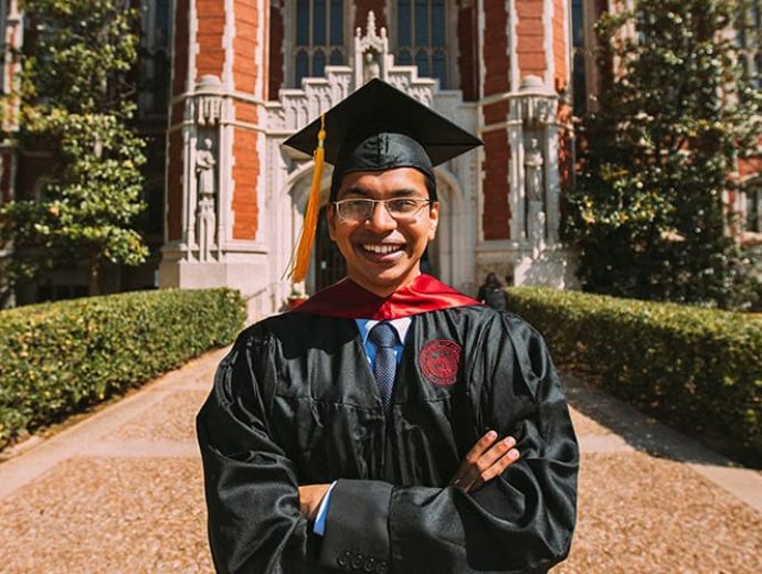 smiling student wearing cap and gown standing in front of Bizzell library